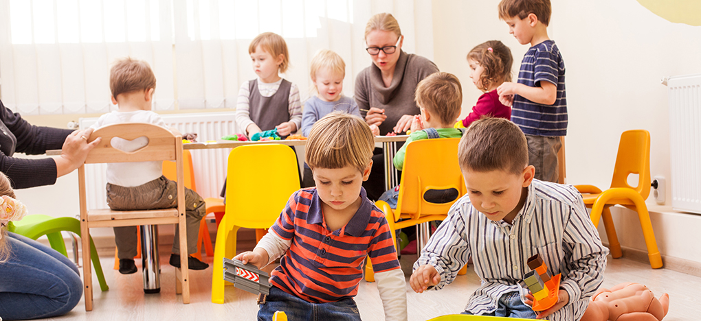 Foto: Eine Erzieherin und Kita-Kinder an Tischen