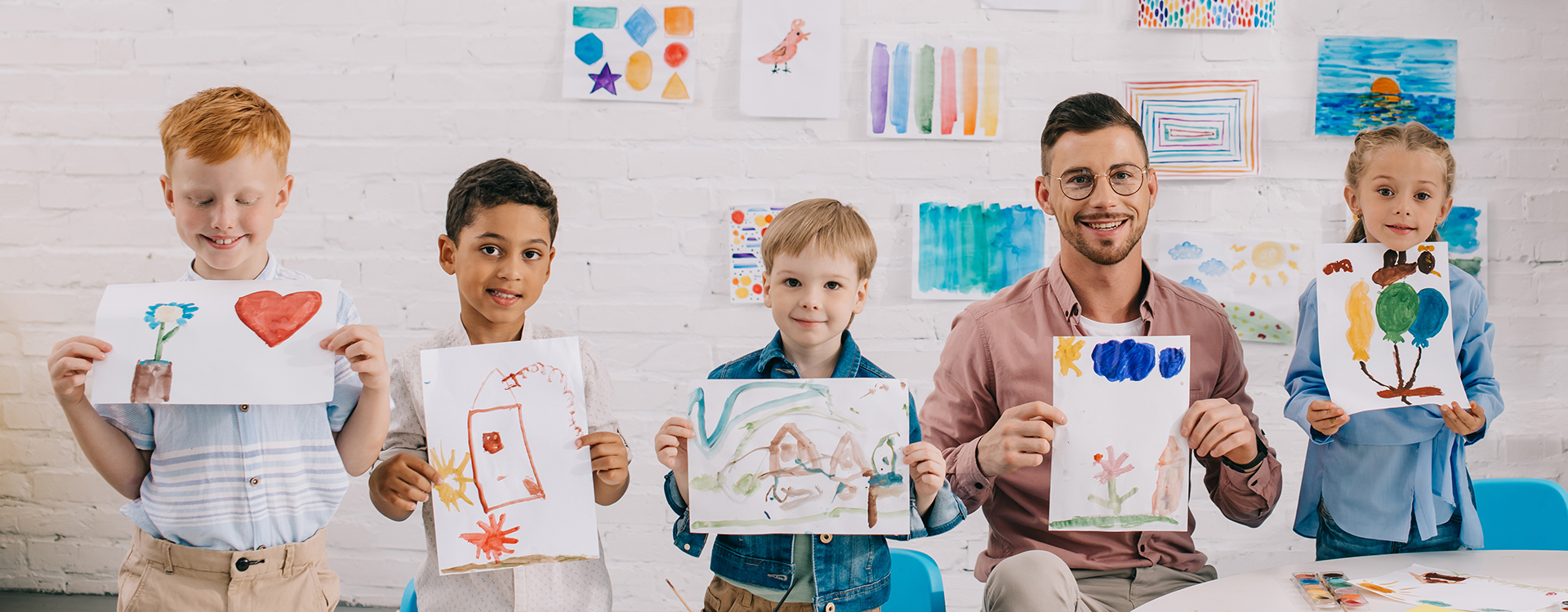 Foto: Erzieher und vier Kinder halten selbst gemalte Bilder hoch