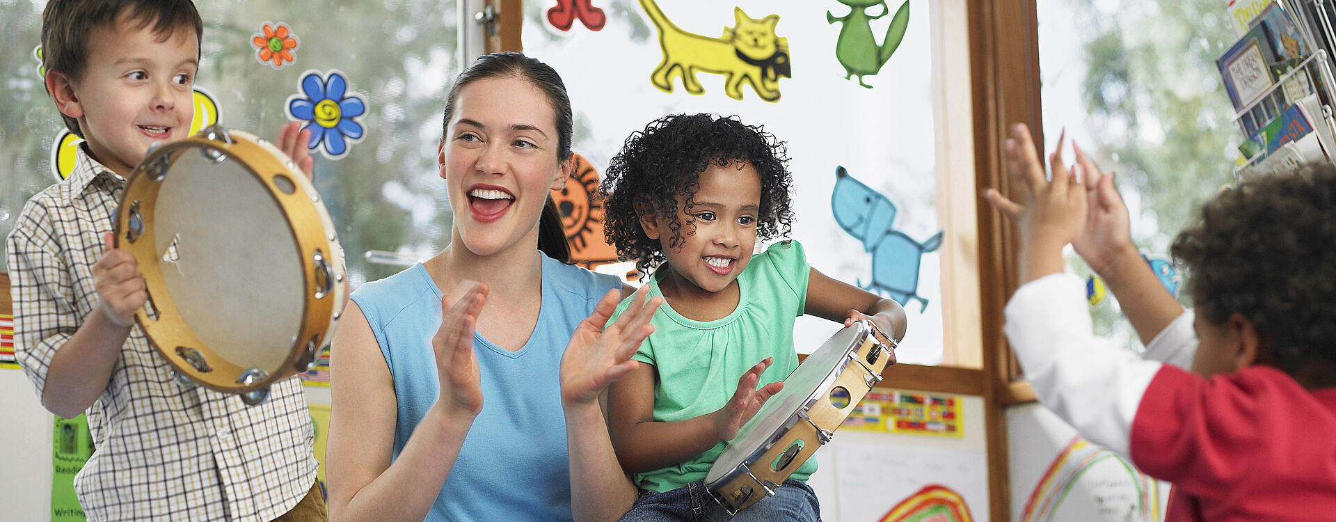 Foto: Eine Erzieherin zusammen mit klatschenden und trommelnden Kindern